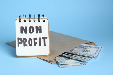 Photo of Notebook with phrase Non Profit and banknotes on light blue background