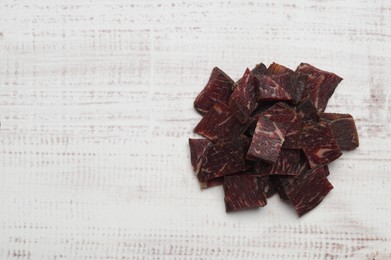 Photo of Delicious beef jerky on white wooden table, top view. Space for text