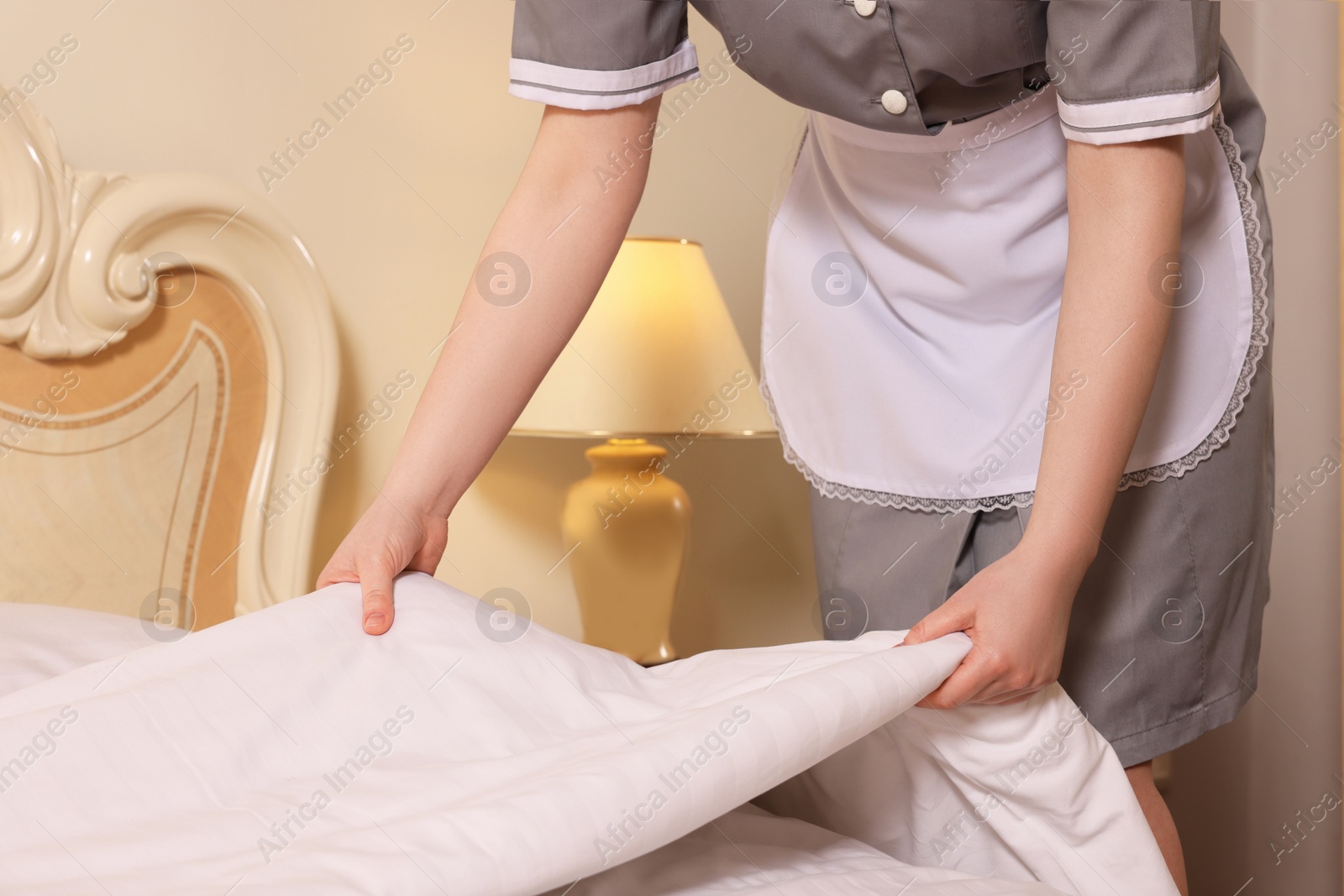 Photo of Young chambermaid making bed in hotel room, closeup