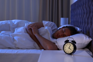 Photo of Alarm clock on nightstand near sleeping young man. Bedtime