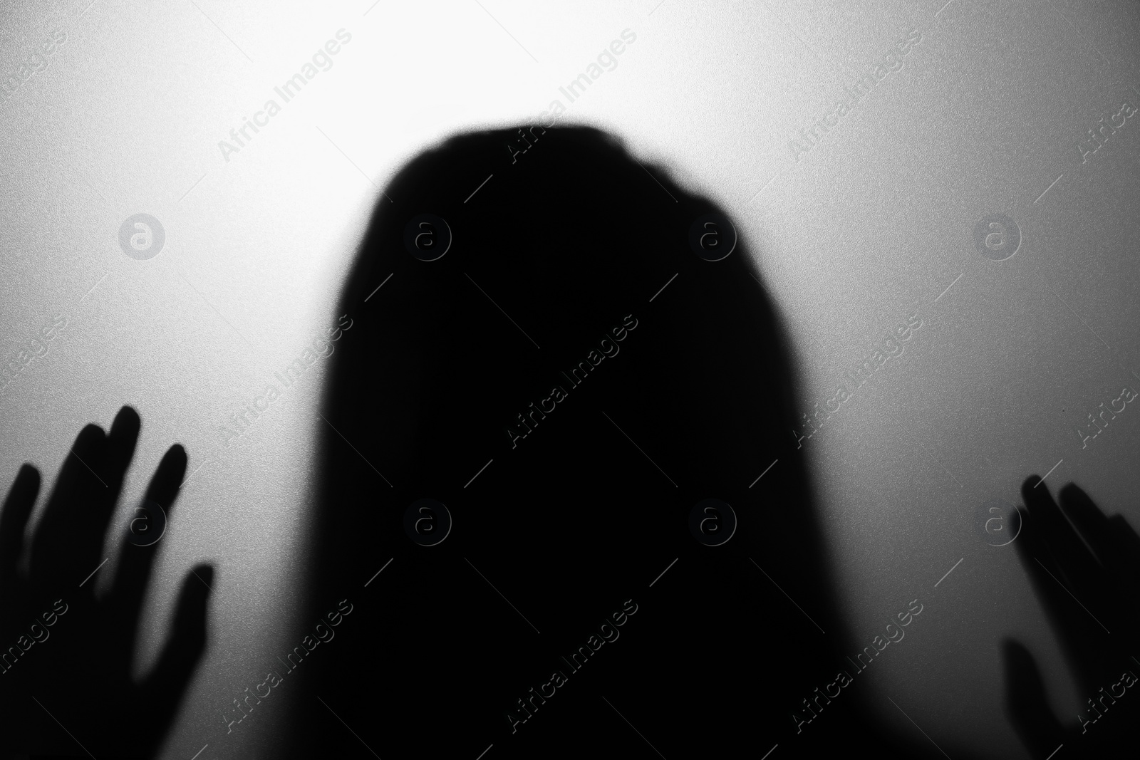 Photo of Silhouette of creepy ghost behind glass against grey background