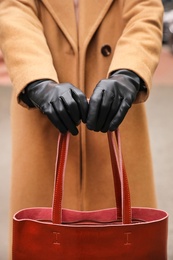 Photo of Young woman in black leather gloves holding red handbag, closeup. Stylish clothes
