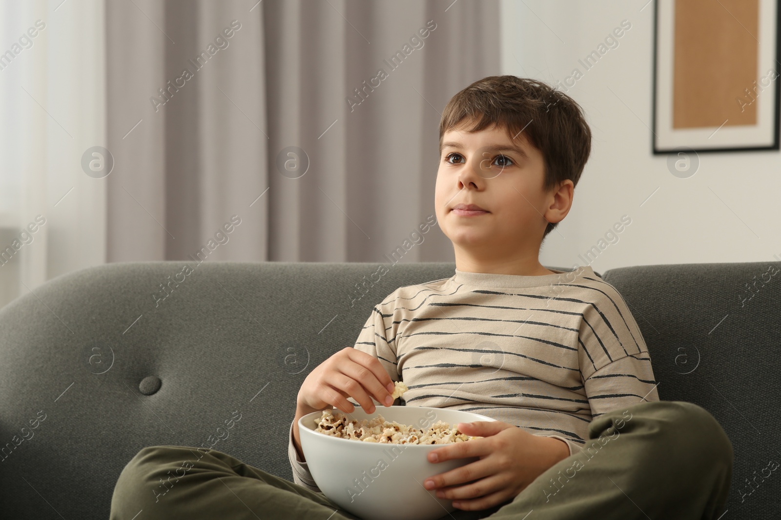 Photo of Little boy eating popcorn while watching TV at home