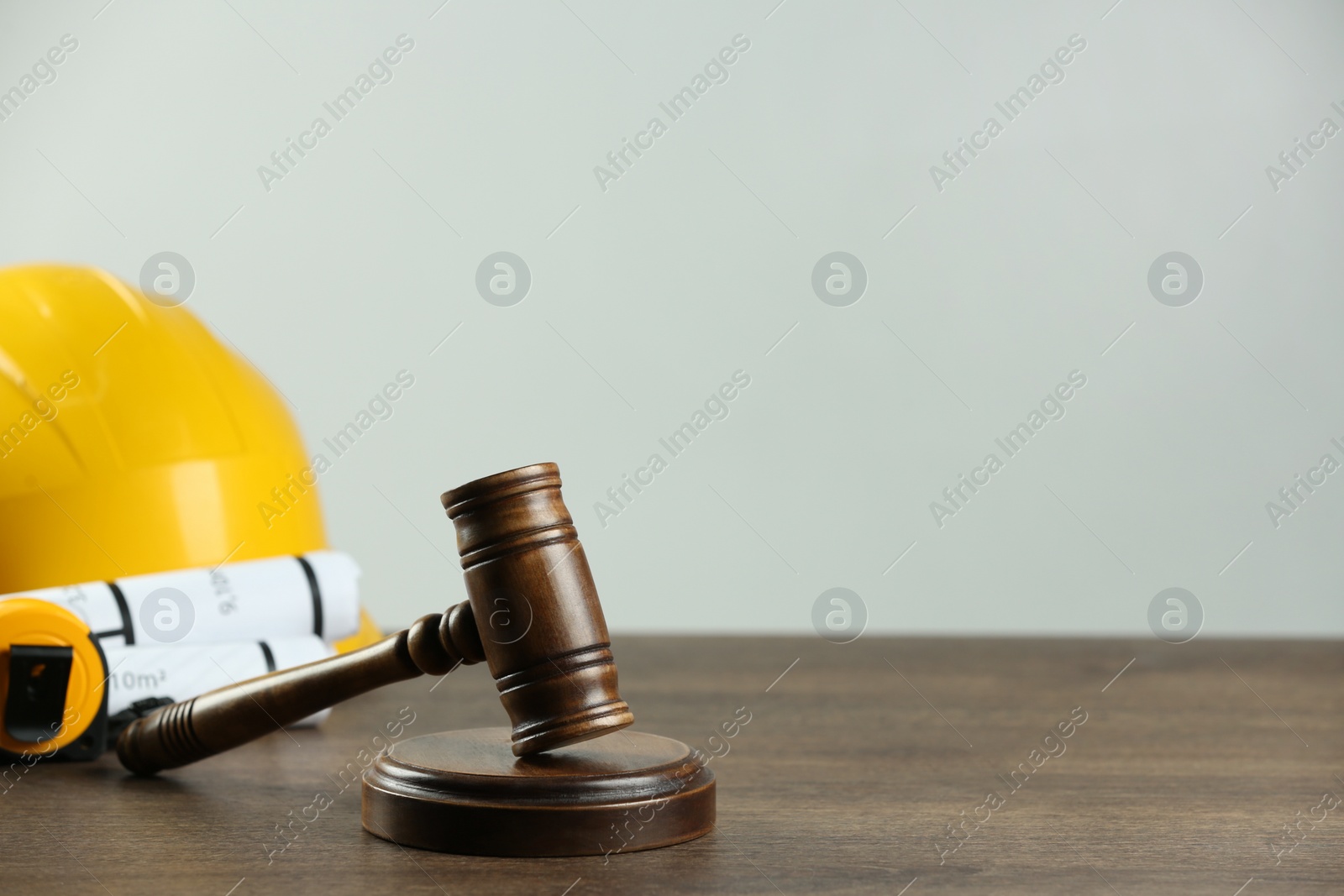 Photo of Construction and land law concepts. Gavel, hard hat, drawings and measuring tape on wooden table, space for text