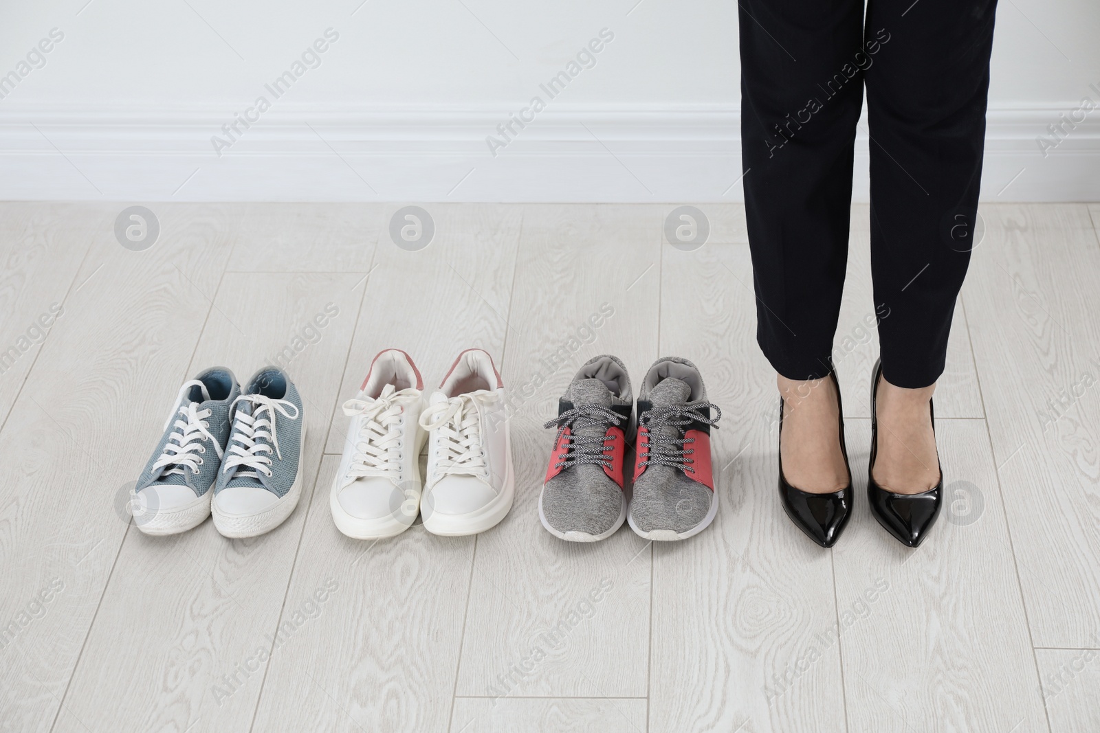 Photo of Different comfortable sneakers near businesswoman wearing high heel shoes indoors, closeup