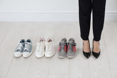 Different comfortable sneakers near businesswoman wearing high heel shoes indoors, closeup