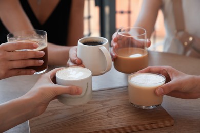 Friends drinking coffee at wooden table in cafe, closeup