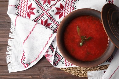 Clay pot with Ukrainian borsch and rushnyk on table, top view