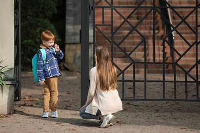 Photo of Little boy waving goodbye to his mother near school