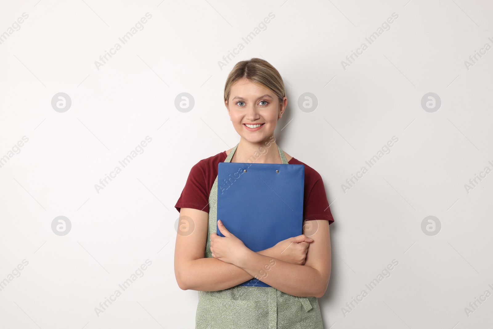 Photo of Beautiful young woman in clean apron with clipboard on light grey background