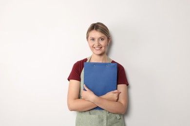 Photo of Beautiful young woman in clean apron with clipboard on light grey background