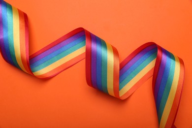 Photo of Rainbow ribbon on orange background, top view. LGBT pride