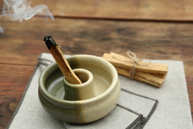 Palo Santo stick smoldering in holder on wooden table