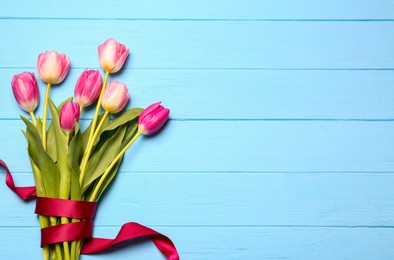 Photo of Beautiful colorful tulip flowers and ribbon on light blue wooden table, top view. Space for text