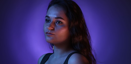 Portrait of beautiful young woman on color background with neon lights