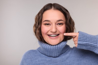 Photo of Happy woman in warm sweater pointing at braces on her teeth against grey background