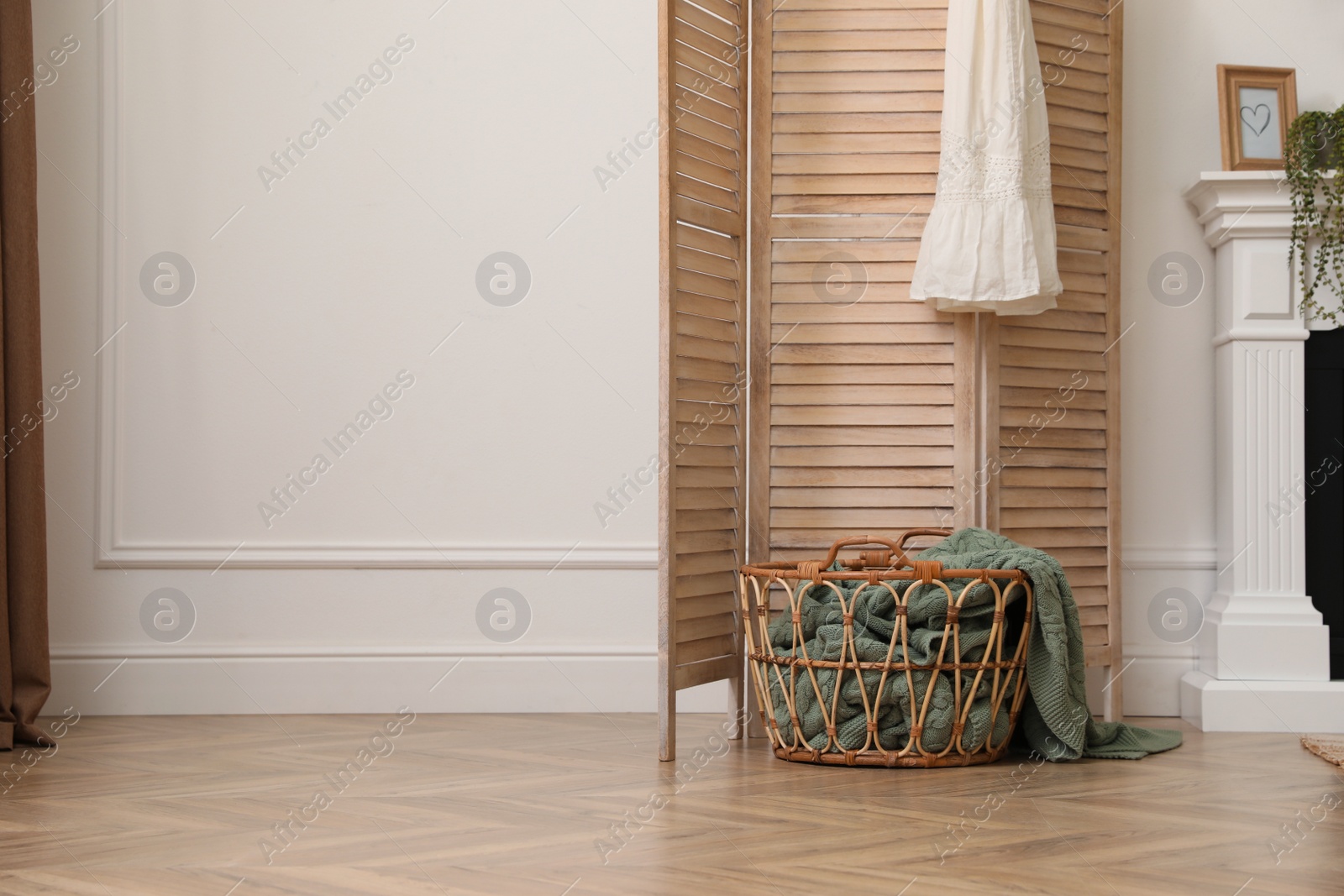 Photo of Wooden folding screen and wicker basket with blanket in room. Interior design