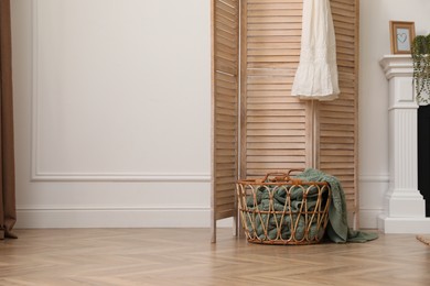 Wooden folding screen and wicker basket with blanket in room. Interior design