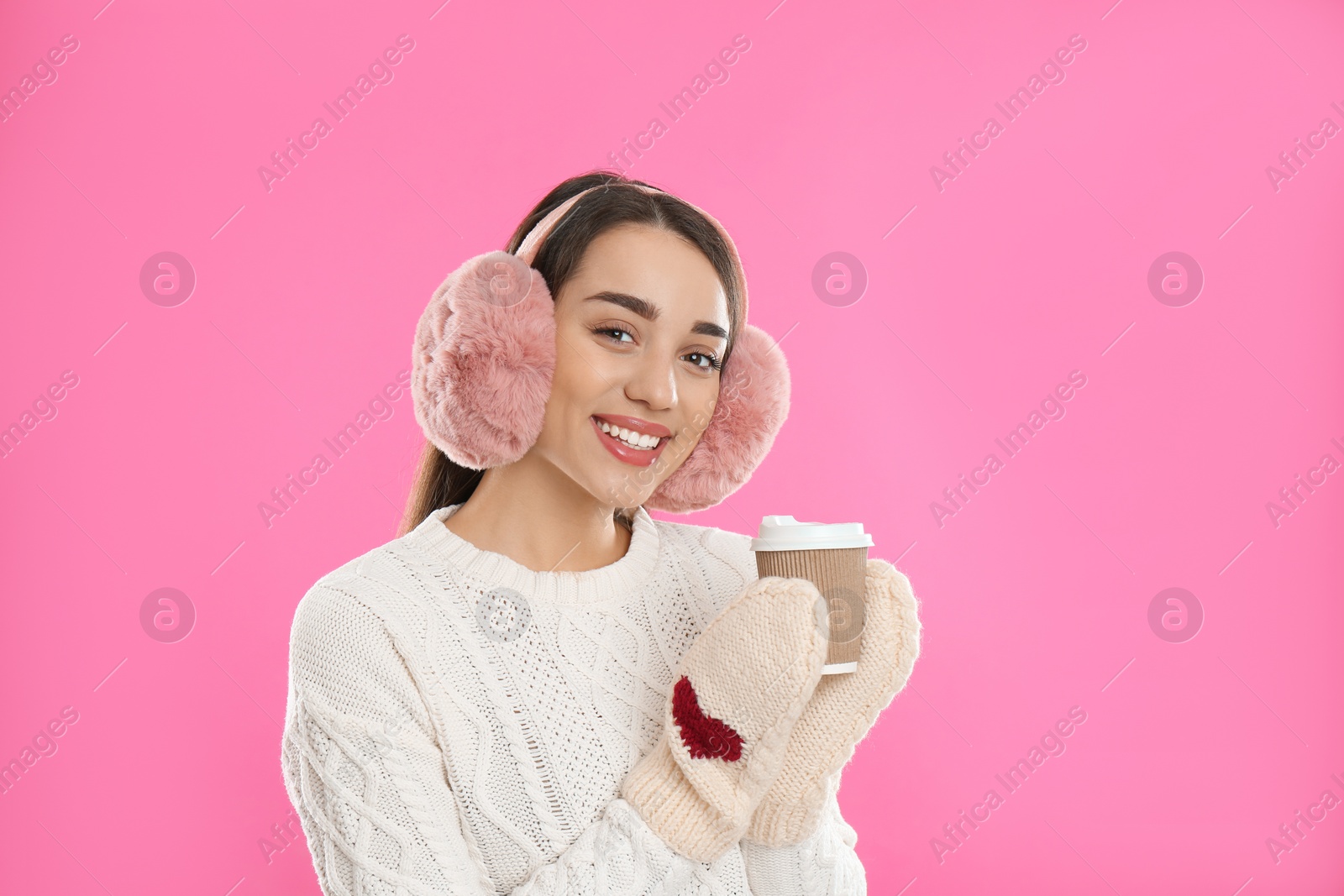 Photo of Beautiful young woman in earmuffs with cup of drink on pink background
