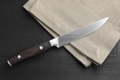 Photo of One sharp knife and napkin on black wooden table, top view