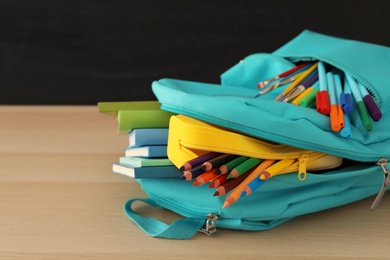 Stylish backpack with different school stationery on wooden table, closeup. Back to school