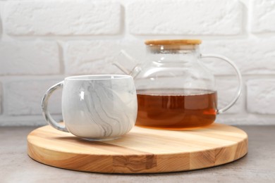 Photo of Aromatic tea in glass teapot and cup on gray table against white brick wall