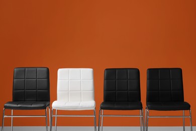 Photo of Black chairs with white one near orange wall, space for text. Recruiter searching employee