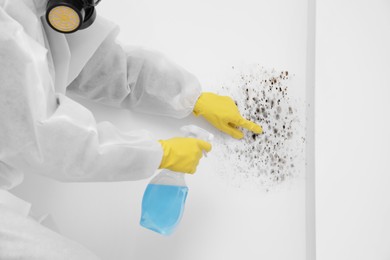 Image of Woman in protective suit and rubber gloves using mold remover on wall, closeup
