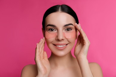 Beautiful young woman with under eye patches on pink background