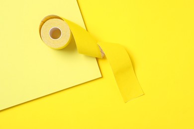 Photo of Bright kinesio tape in roll on yellow background, top view
