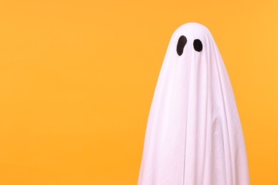 Child in white ghost costume on orange background, space for text. Halloween celebration