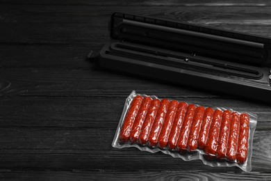 Photo of Vacuum packing sealer and plastic bag of sausages on black wooden table, space for text