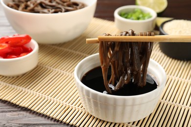 Photo of Eating delicious buckwheat noodles (soba) with chopsticks at wooden table, closeup. Space for text