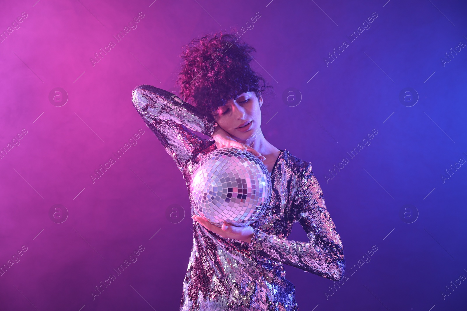 Photo of Beautiful young woman with disco ball posing on color background in neon lights