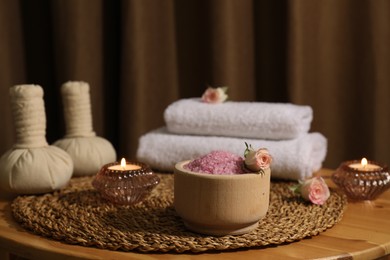 Photo of Bowl of pink sea salt, roses, burning candles and towels on wooden table