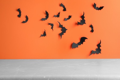 Photo of Empty grey table near orange wall decorated with paper bats. Halloween celebration