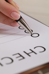Photo of Woman filling Checklist with pen at table, closeup view