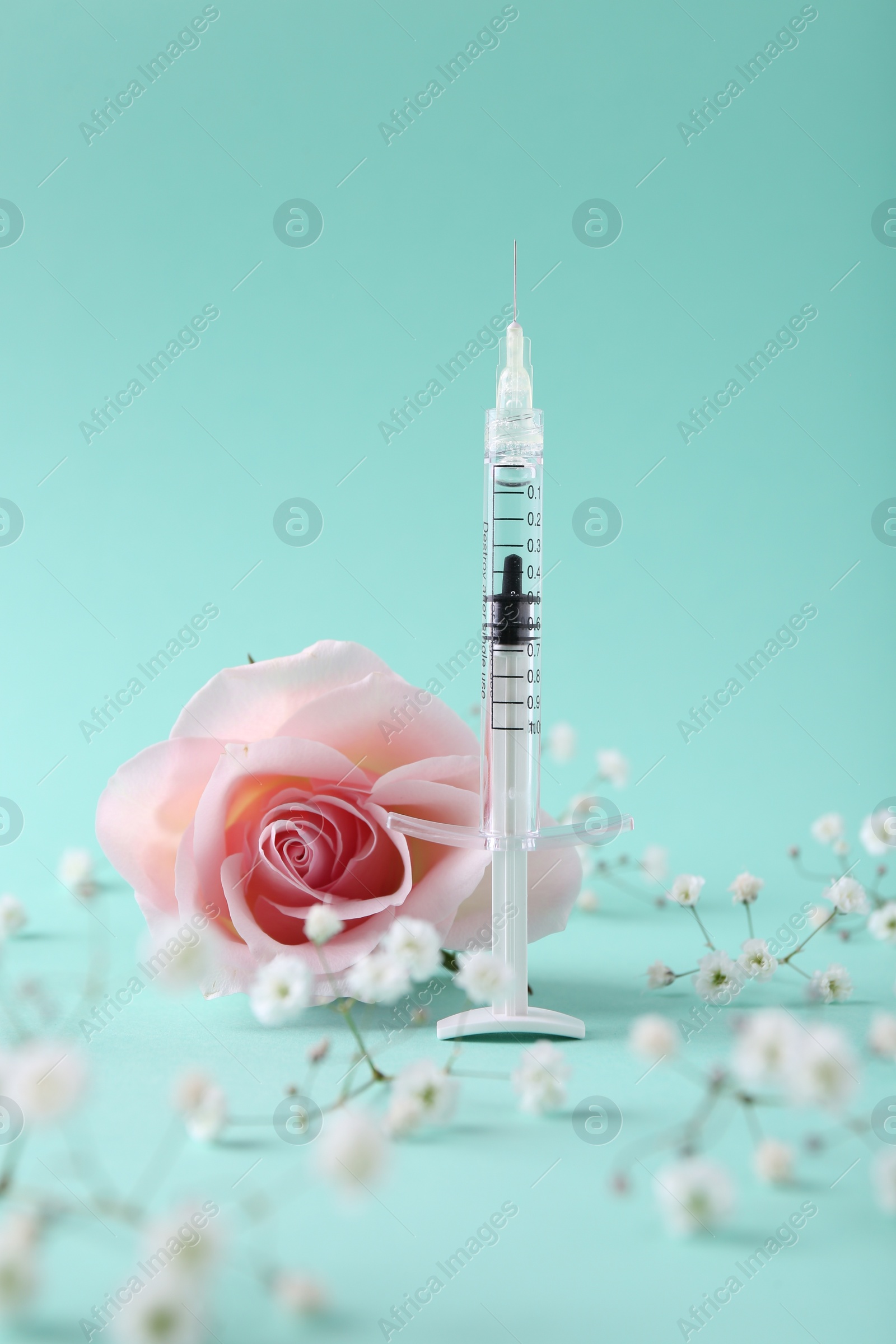 Photo of Cosmetology. Medical syringe, rose and gypsophila flowers on turquoise background