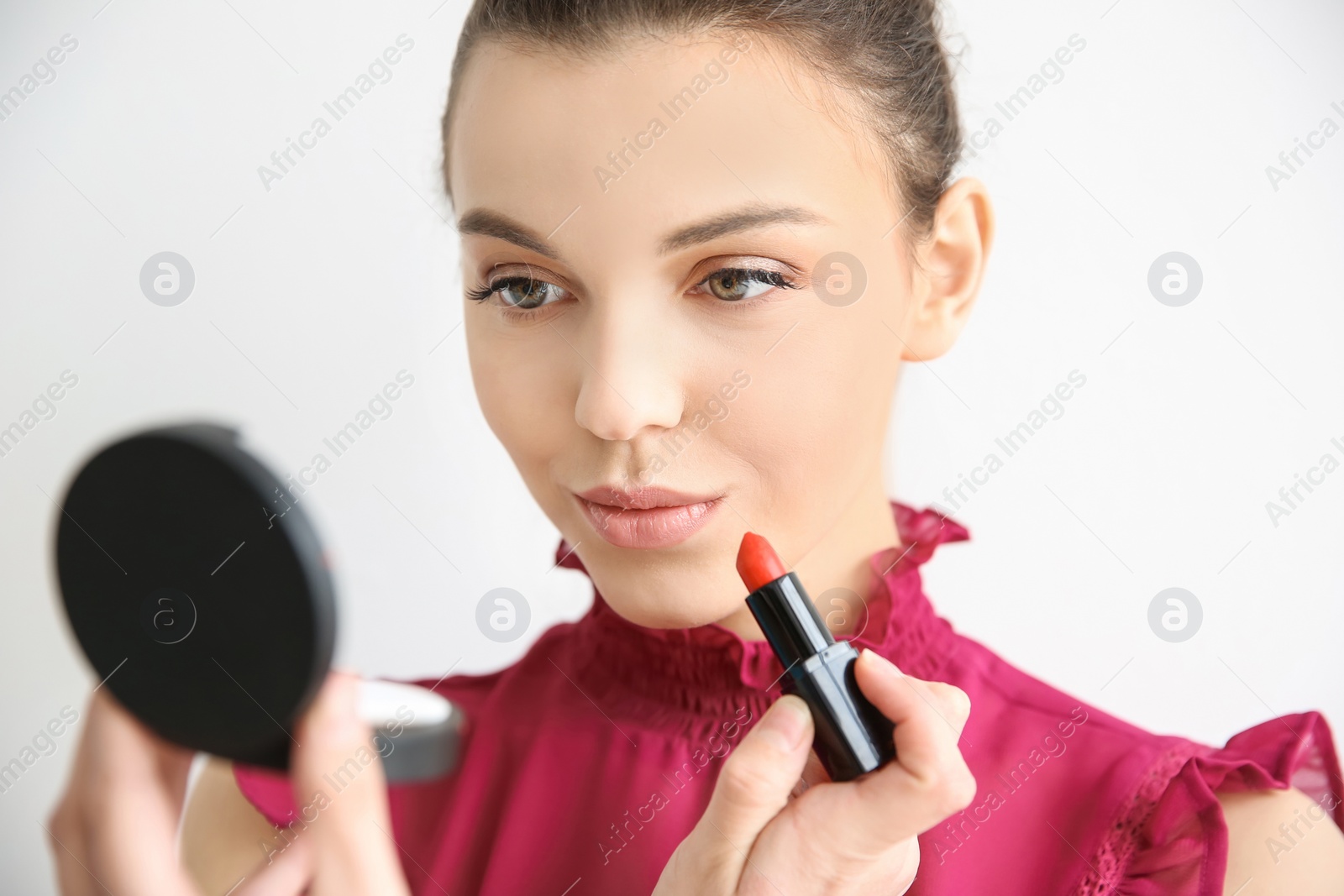 Photo of Young woman applying lipstick on light background. Professional makeup products