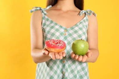 Photo of Concept of choice. Woman holding apple and doughnut on yellow background, closeup