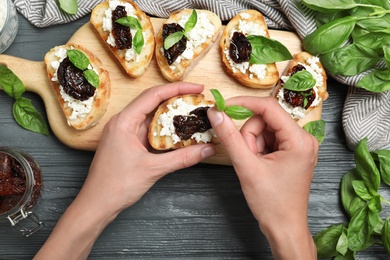Photo of Woman preparing bruschetta with dried tomatoes at dark grey wooden table, top view