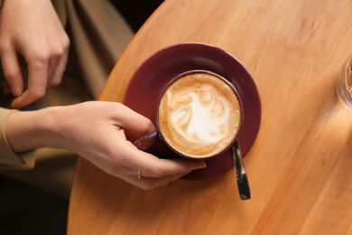 Woman with cup of aromatic coffee at table in cafe, top view