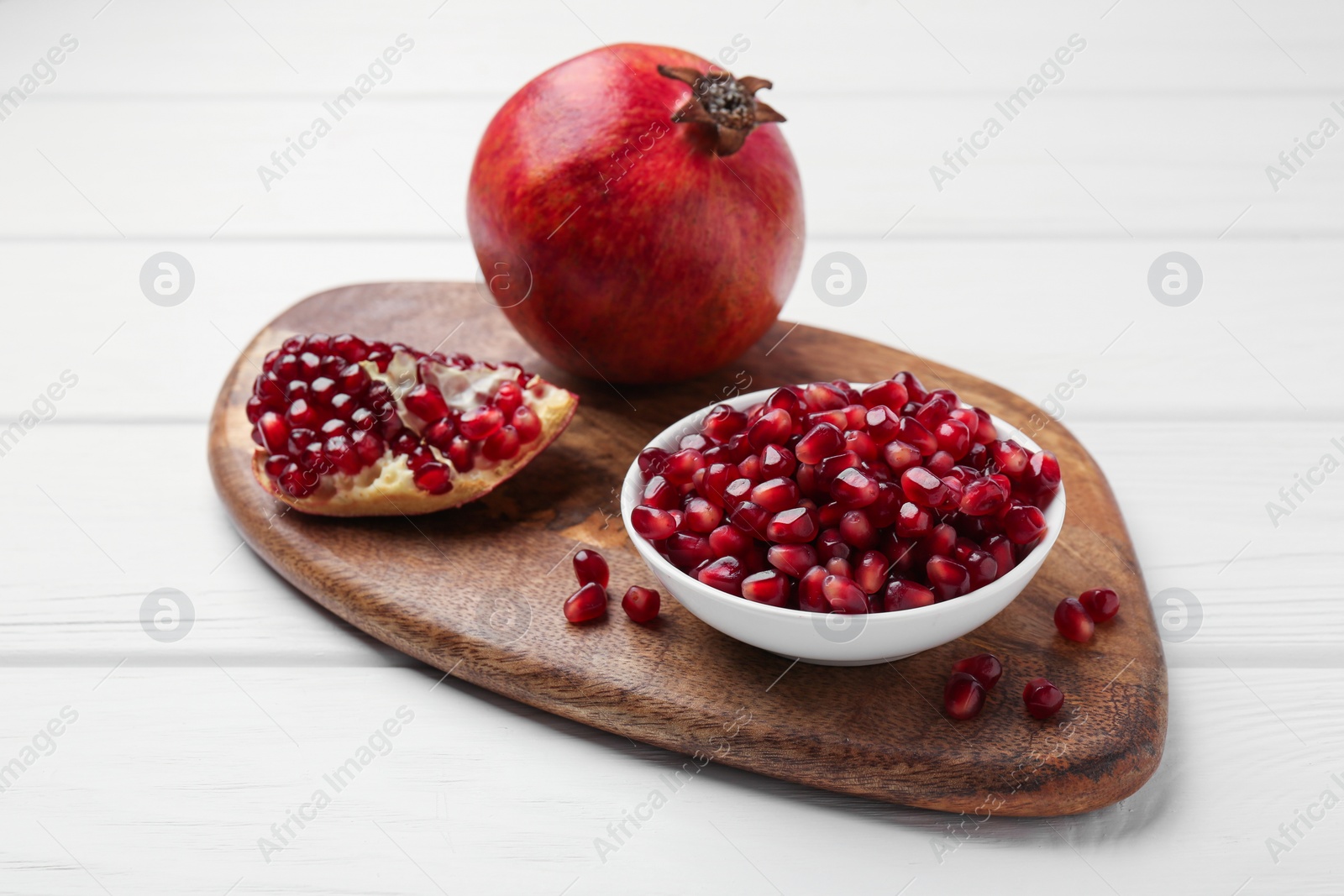 Photo of Ripe juicy pomegranate with grains on white wooden table