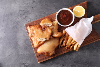 Photo of Tasty fish, chips and sauce on grey table, top view. Space for text