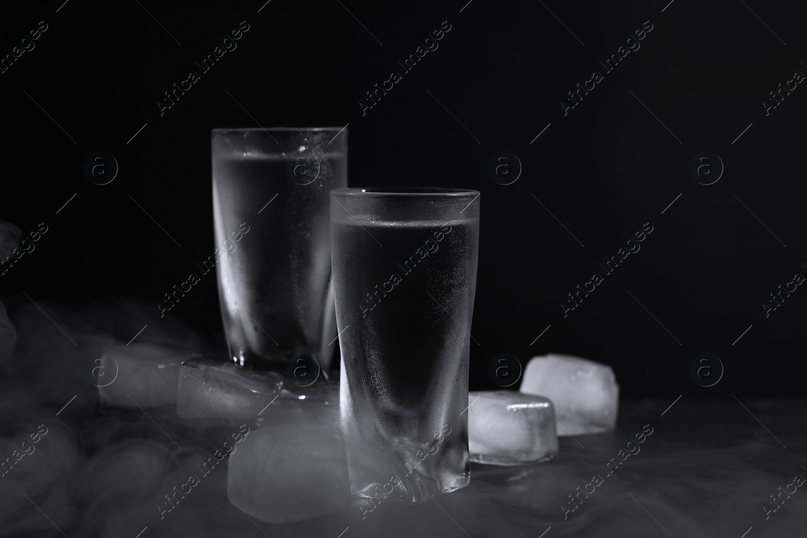 Photo of Vodka in shot glasses with ice on table against black background