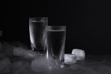 Photo of Vodka in shot glasses with ice on table against black background
