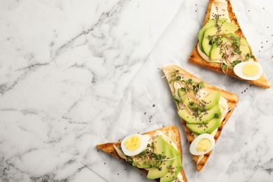 Photo of Tasty toasts with avocado, quail eggs and chia seeds on marble background, top view. Space for text