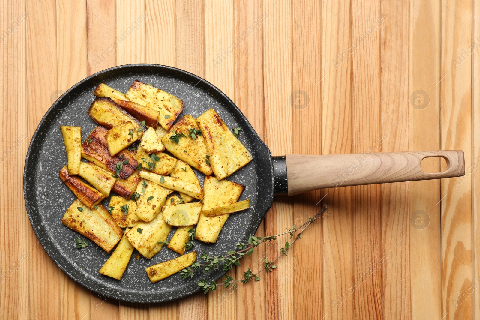 Photo of Delicious parsnips with thyme in frying pan on wooden table, top view