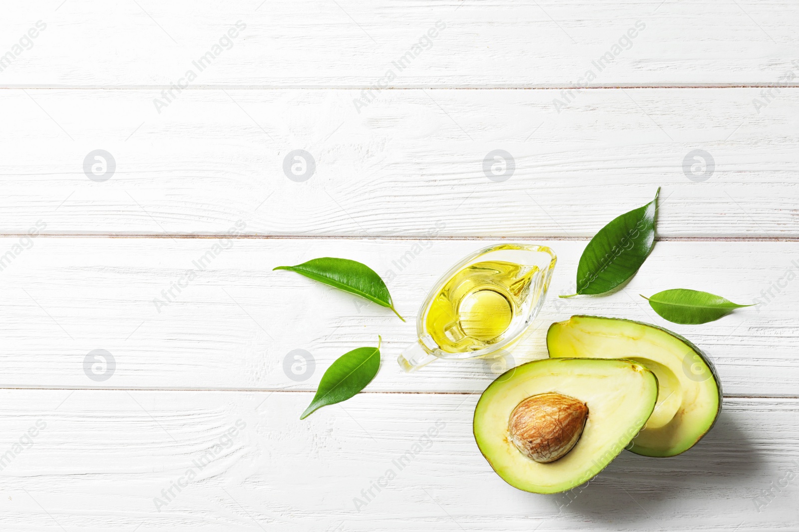 Photo of Gravy boat with oil and ripe fresh avocado on wooden table, top view