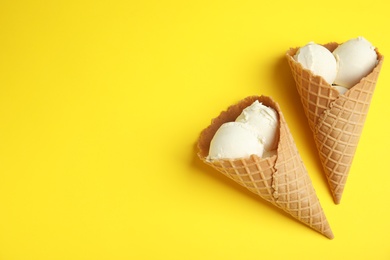 Photo of Delicious vanilla ice cream in wafer cones on yellow background, flat lay. Space for text